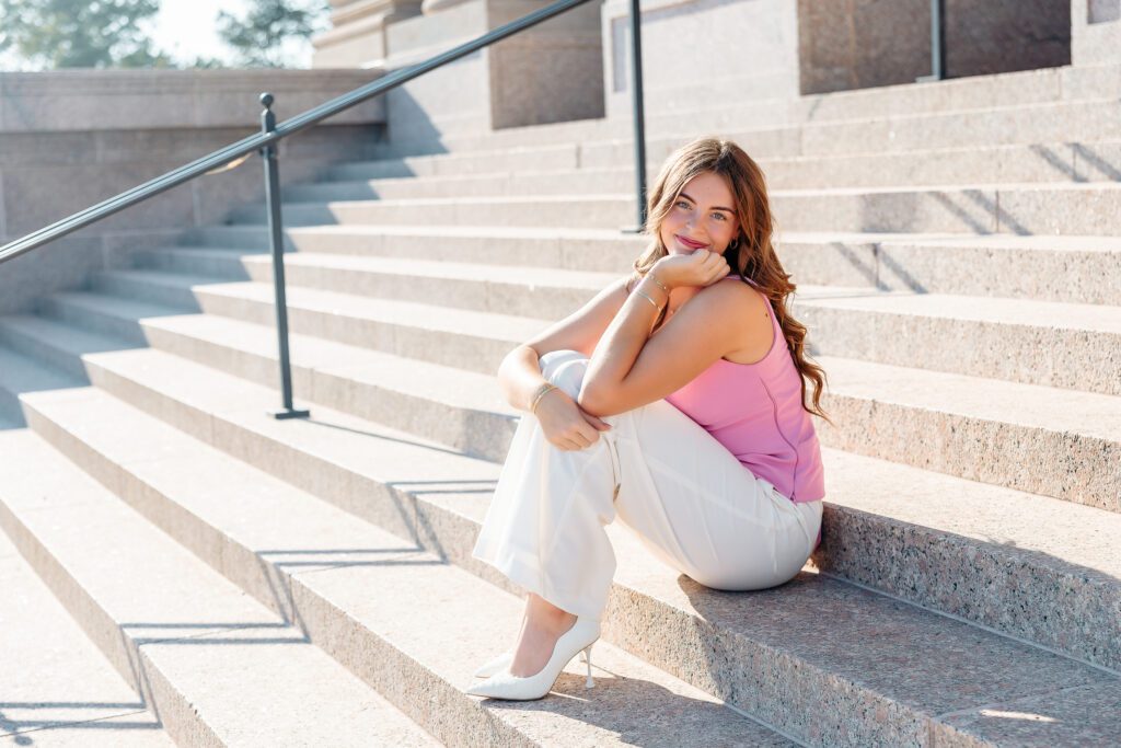 Senior girl in pink top sitting on stairs at the state capitol in Oklahoma City. Photo taken by Ellie Piper from Ellie Piper Photography